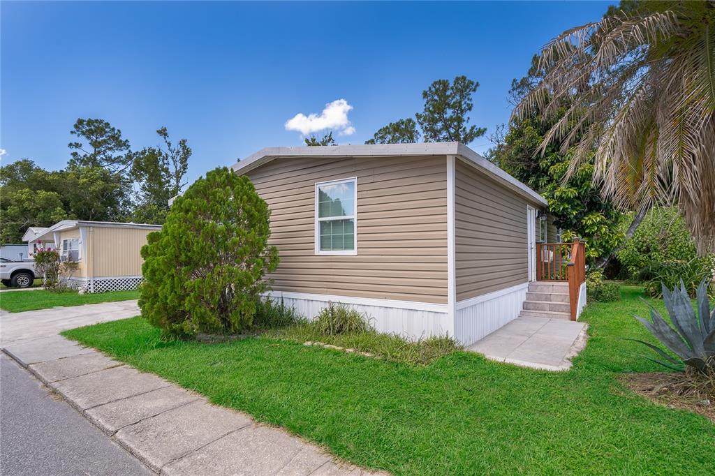 A tan mobile home with horizontal siding and a small wooden porch sits on grass — 1838 ANNAPOLIS AVENUE, ORLANDO, FL