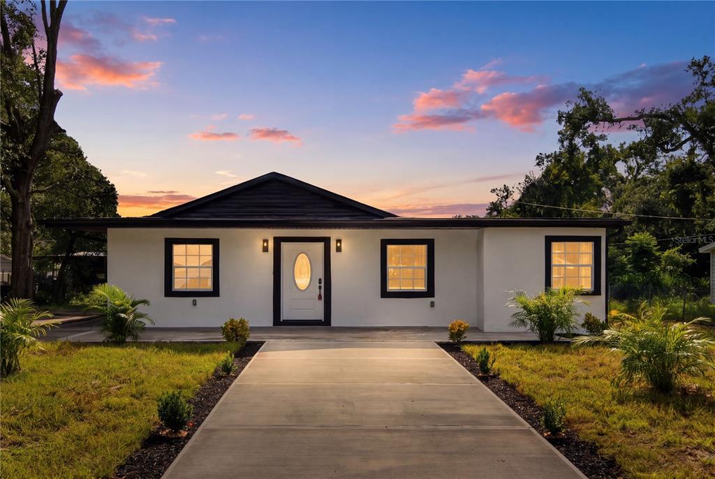 A single-story white house with a dark roof and black window frames faces a concrete walkway — 3619 N 72ND STREET, TAMPA, FL