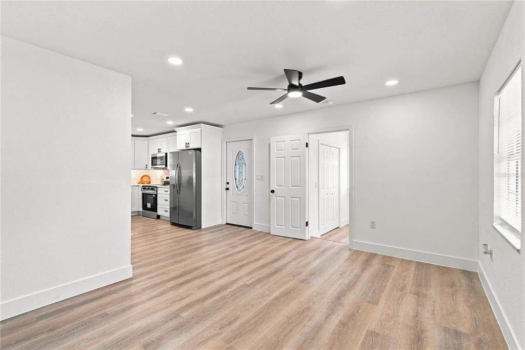 A bright room features light wood-look flooring, a ceiling fan, and an adjacent kitchen area — 3619 N 72ND STREET, TAMPA, FL