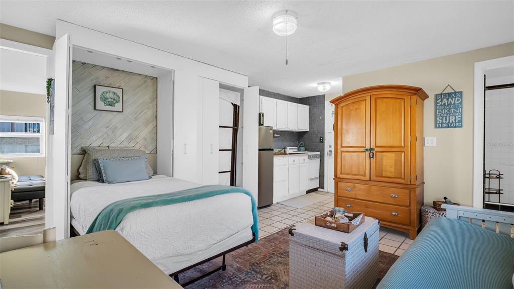 A bedroom features a wooden armoire, a futon with a teal throw, and a white door — 483 E SHORE DRIVE UNIT D4, CLEARWATER BEACH, FL
