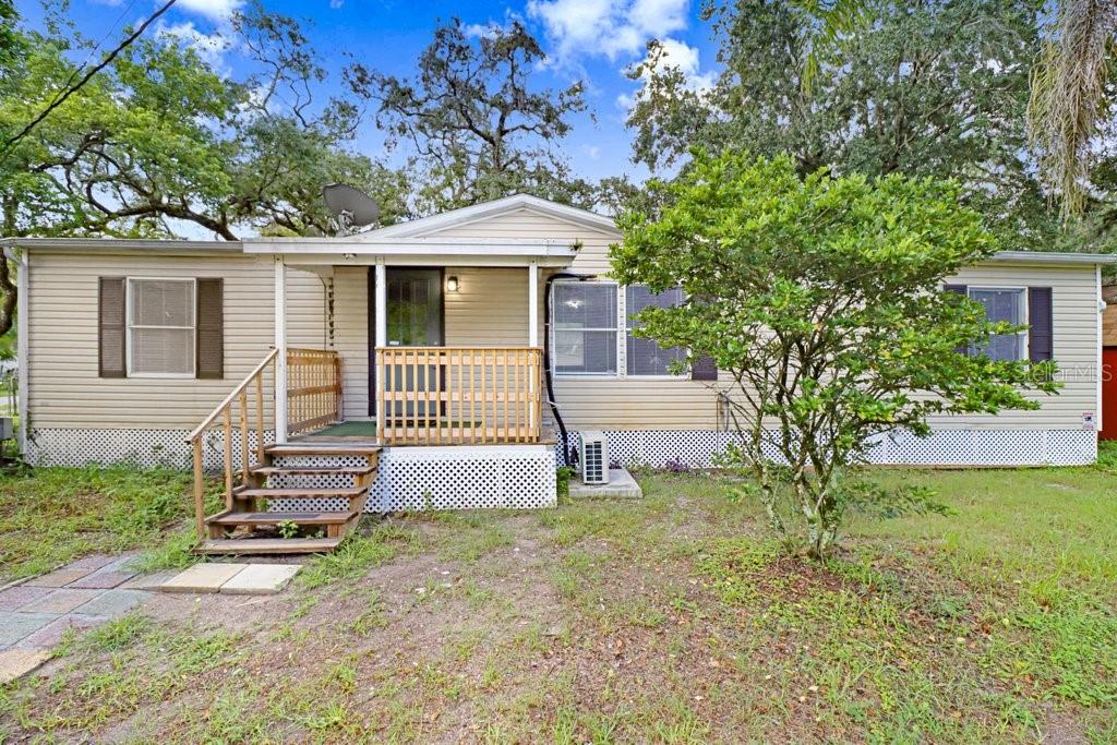 A single-story mobile home with tan siding, a wooden front porch, and a small tree — 12610 ALEMEDO AVENUE, NEW PORT RICHEY, FL