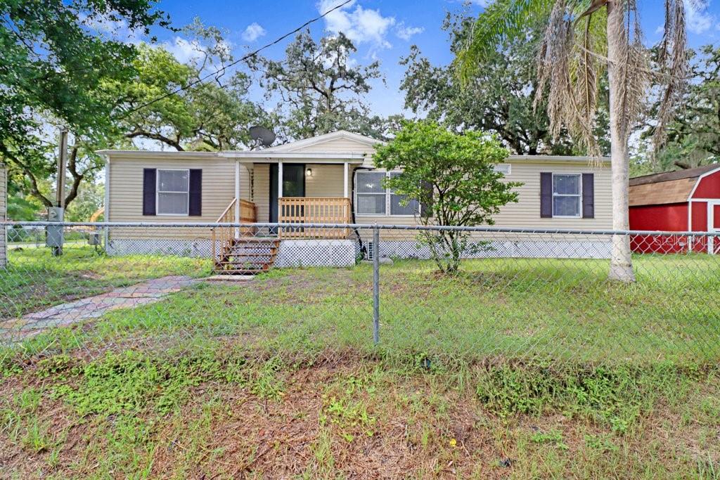 A single-story tan mobile home with a front porch sits behind a chain-link fence — 12610 ALEMEDO AVENUE, NEW PORT RICHEY, FL