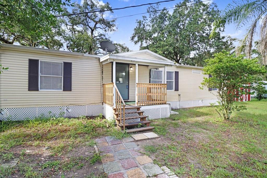 A single-story mobile home with beige siding, a front porch, and a stone walkway — 12610 ALEMEDO AVENUE, NEW PORT RICHEY, FL