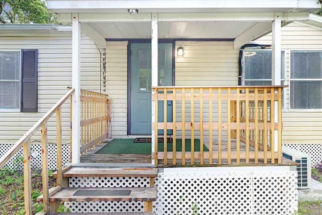 A wooden porch with railings and stairs leads to the front door of a house — 12610 ALEMEDO AVENUE, NEW PORT RICHEY, FL