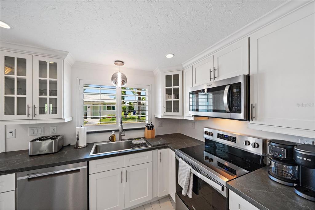 A kitchen features white cabinetry, stainless steel appliances, dark countertops, and a window over the sink — 706 SPANISH DRIVE S, LONGBOAT KEY, FL
