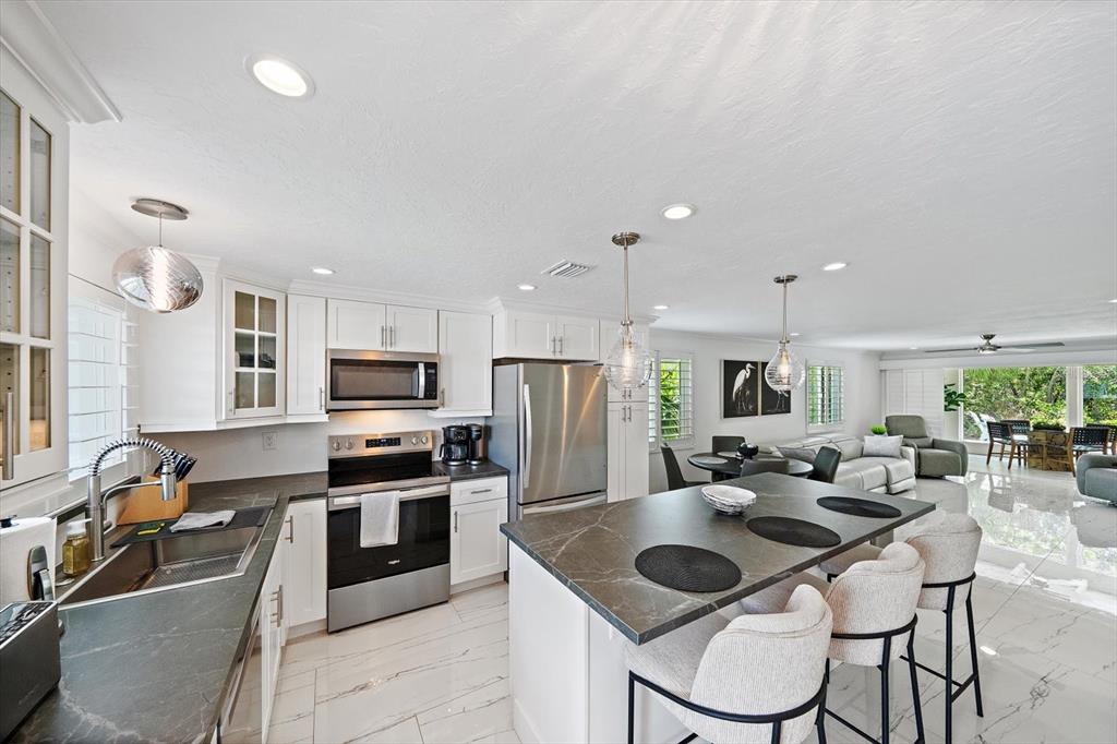 A modern kitchen features white cabinetry, stainless steel appliances, and a dark stone-topped island — 706 SPANISH DRIVE S, LONGBOAT KEY, FL