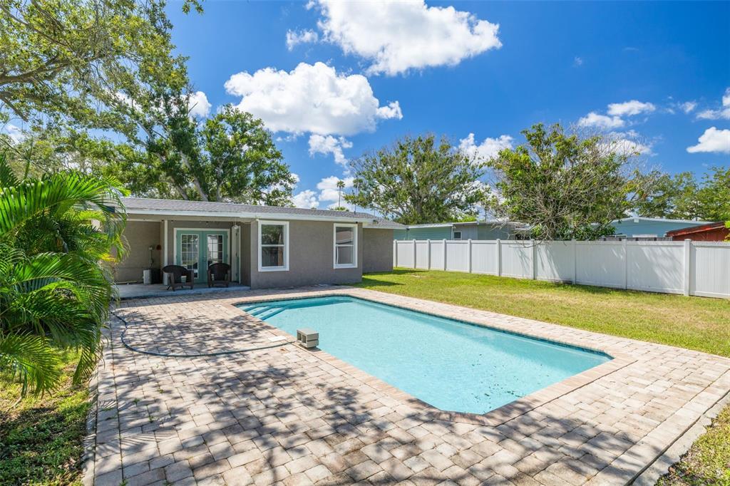 A backyard features a rectangular swimming pool, a brick paver patio, and a white privacy fence — 4227 HARRISBURG STREET NE, ST PETERSBURG, FL