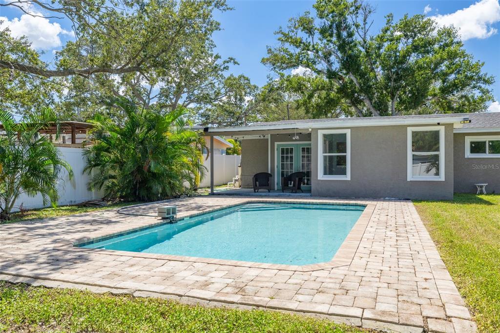 A backyard features a rectangular swimming pool with a brick paver deck and a covered patio — 4227 HARRISBURG STREET NE, ST PETERSBURG, FL