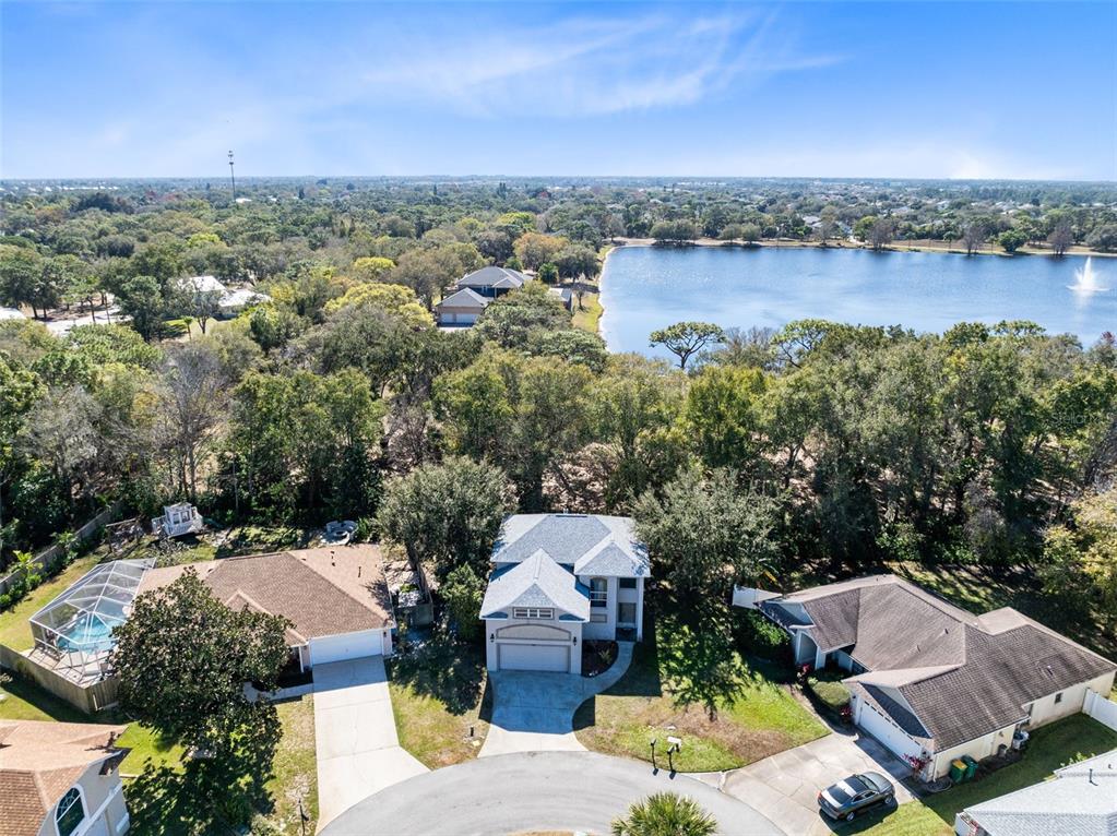 An aerial view shows three suburban houses with driveways near a lake and trees — 703 SAMUEL CHASE LANE, WEST MELBOURNE, FL