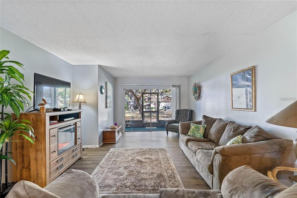 A living room features a fireplace console, brown sofa, area rug, and sliding glass doors — 870 VIRGINIA STREET UNIT 104, DUNEDIN, FL