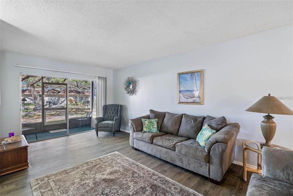 A living room features gray wood-look flooring, a gray sofa, and a sliding glass door — 870 VIRGINIA STREET UNIT 104, DUNEDIN, FL