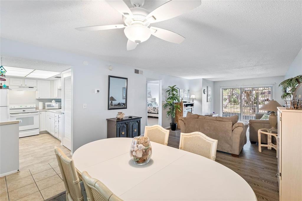 A dining area opens into a living room with a ceiling fan and sliding glass doors — 870 VIRGINIA STREET UNIT 104, DUNEDIN, FL