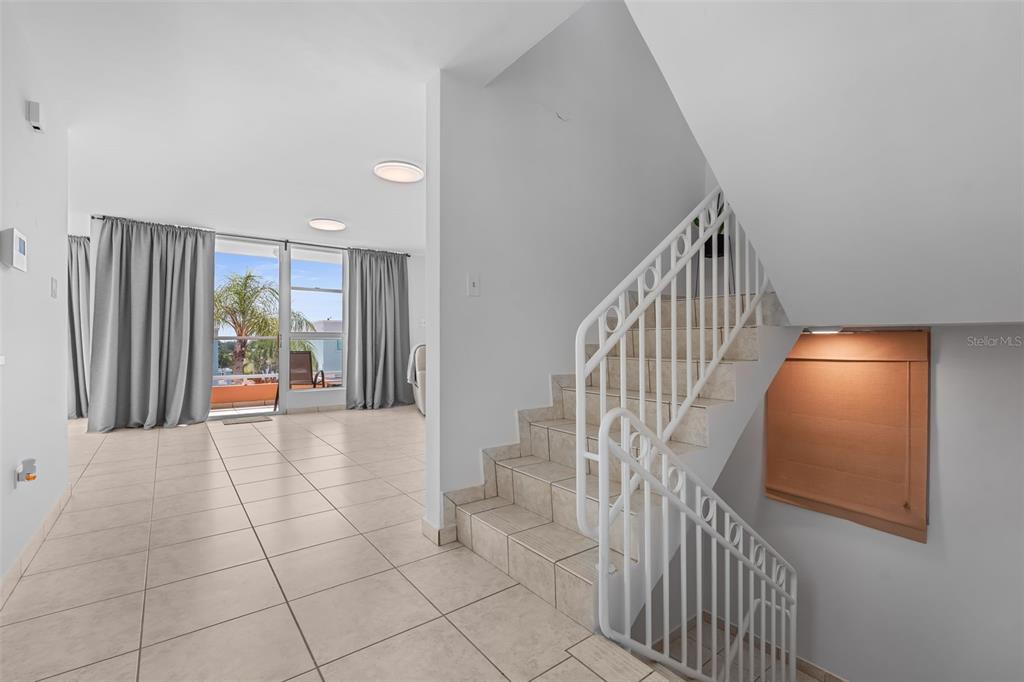 A tiled room features a white staircase with a metal railing and a sliding glass door — 65 THE VILLAGE AT THE HILL, CEIBA, PR