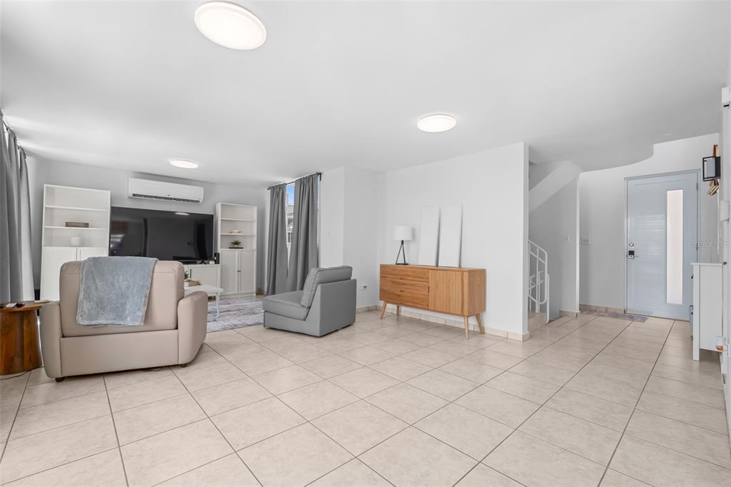 A bright living room features light tile floors, white walls, and a modern entryway door — 65 THE VILLAGE AT THE HILL, CEIBA, PR