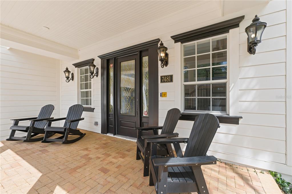 A covered brick porch features four black Adirondack chairs and a dark-framed front door — 7481 GATHERING LOOP, REUNION, FL
