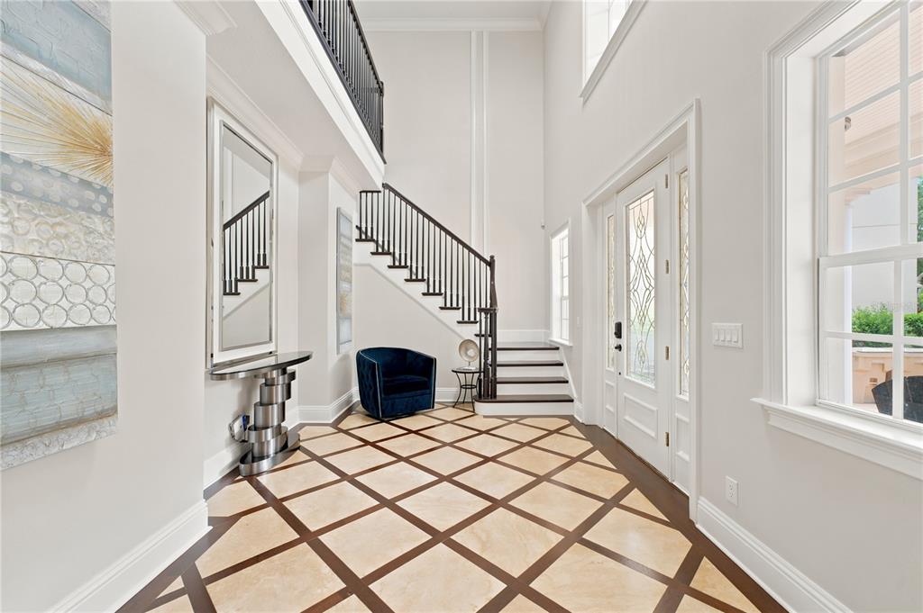 A bright foyer features a diamond-patterned floor, a dark staircase, and a blue accent chair — 7481 GATHERING LOOP, REUNION, FL