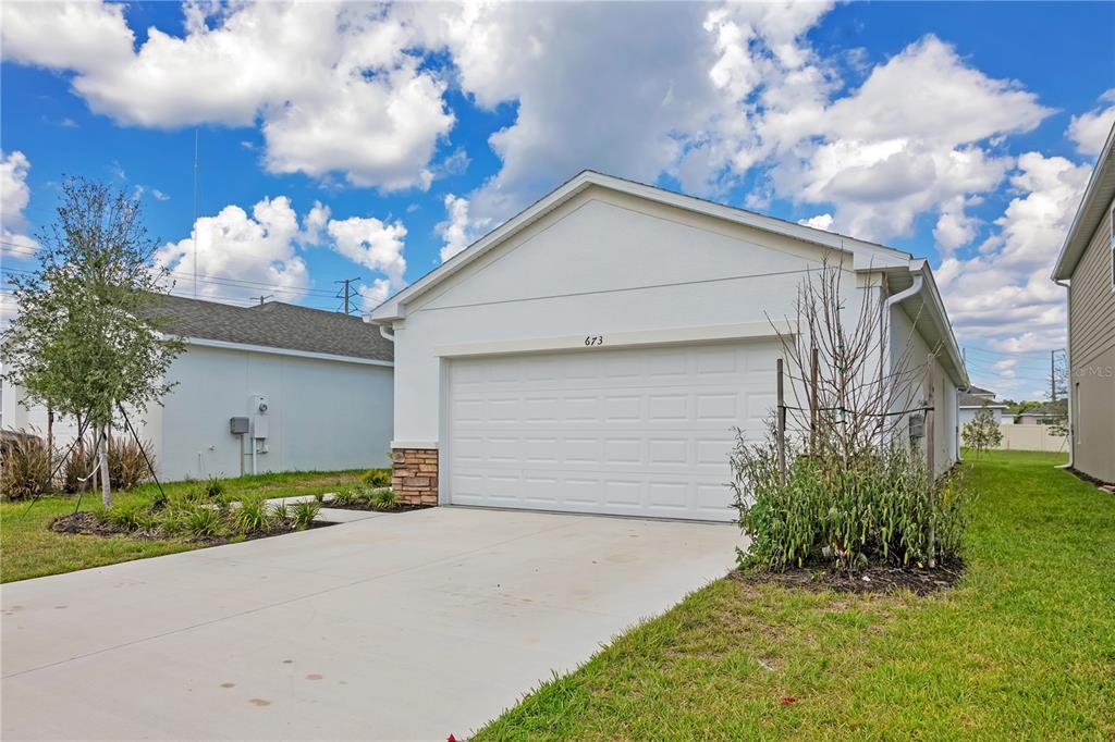 A white single-story house exterior features a two-car garage, stone accents, and a concrete driveway — 673 TEVIOT ROAD, HAINES CITY, FL