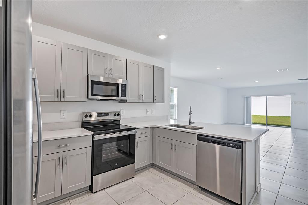 A modern kitchen features light gray cabinets, stainless steel appliances, and white countertops — 673 TEVIOT ROAD, HAINES CITY, FL