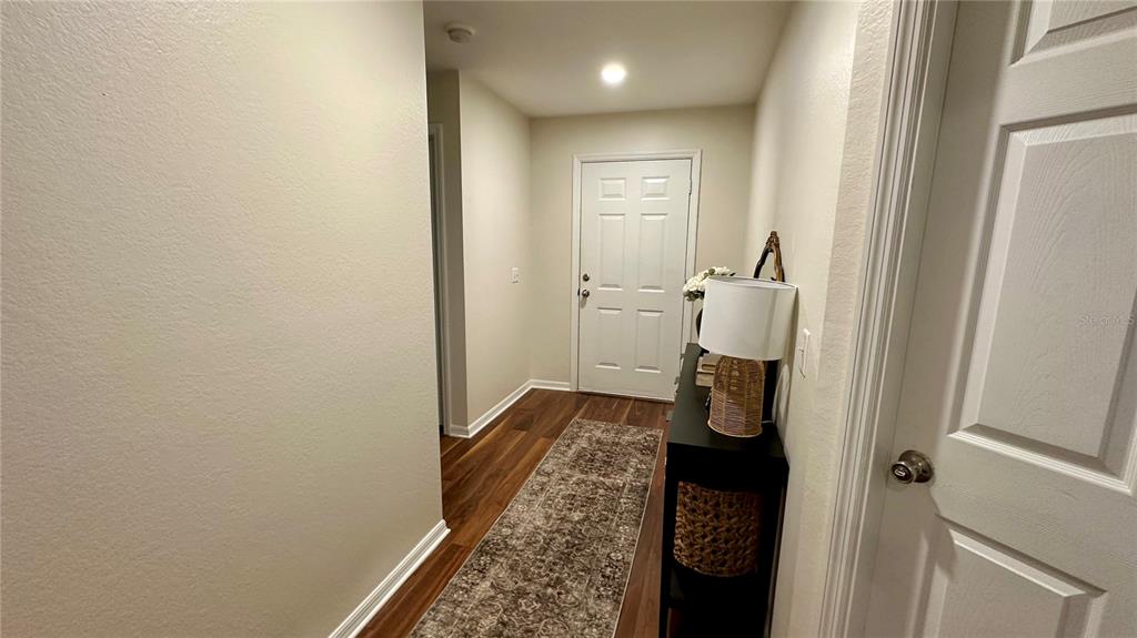 An entryway features wood-look flooring, a runner rug, a console table, and a white door — 906 SE 5TH STREET, MULBERRY, FL