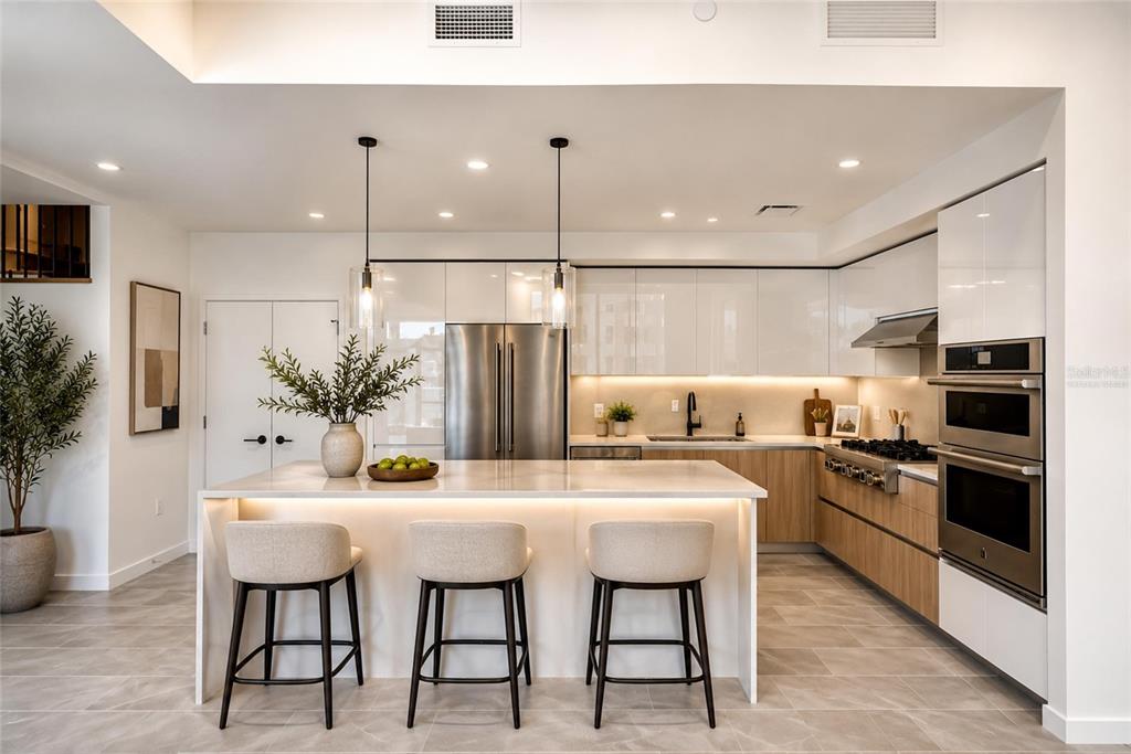 A modern kitchen features white glossy cabinets, wood-toned lower cabinets, a large island, and stainless appliances — 400 CENTRAL AVENUE UNIT 407, ST PETERSBURG, FL