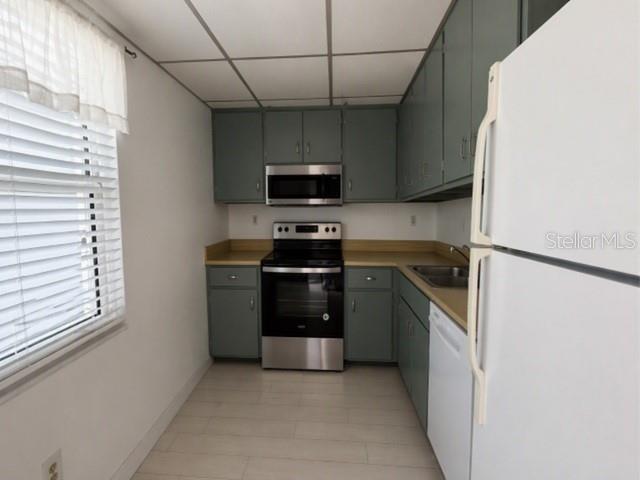 A galley kitchen features gray cabinets, stainless steel appliances, and light-colored flooring — 1740 PINE VALLEY DRIVE UNIT 205, FORT MYERS, FL