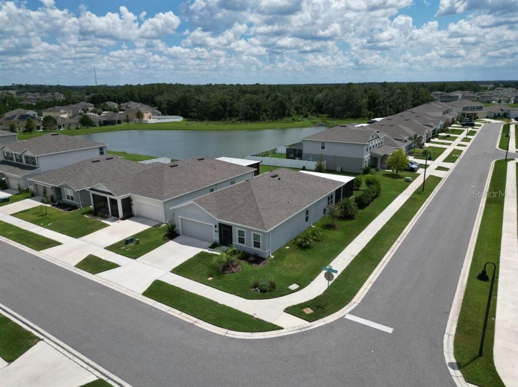 An aerial view shows suburban houses with gray roofs situated near a pond and street — 6650 PEBBLEBROOKE WAY, ZEPHYRHILLS, FL