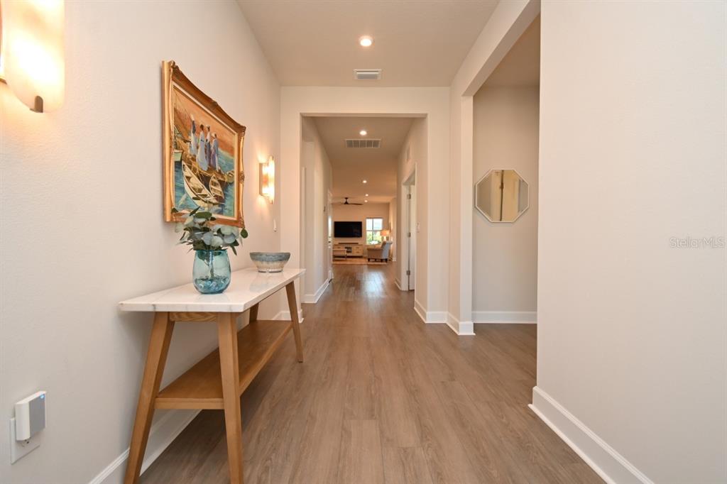 A hallway with light wood flooring, a marble-topped console table, and a framed painting — 6650 PEBBLEBROOKE WAY, ZEPHYRHILLS, FL