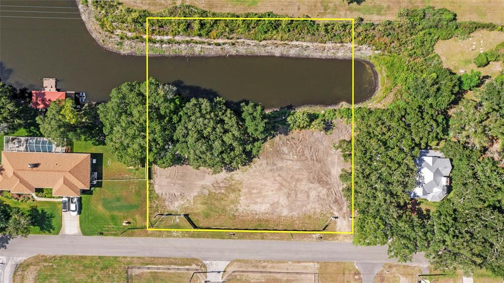 An aerial view shows a vacant, cleared rectangular lot situated between a road and a canal — 5030 DUQUE ROAD, LUTZ, FL