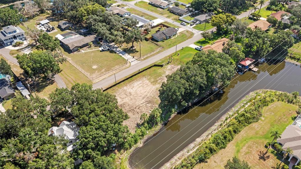 An aerial view shows a vacant, cleared lot situated between a residential street and a canal — 5030 DUQUE ROAD, LUTZ, FL