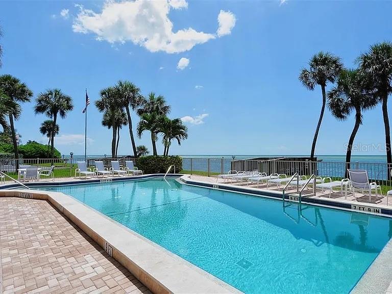 A swimming pool sits on a patio overlooking the ocean with palm trees nearby — 4822 OCEAN BOULEVARD UNIT 3D, SARASOTA, FL