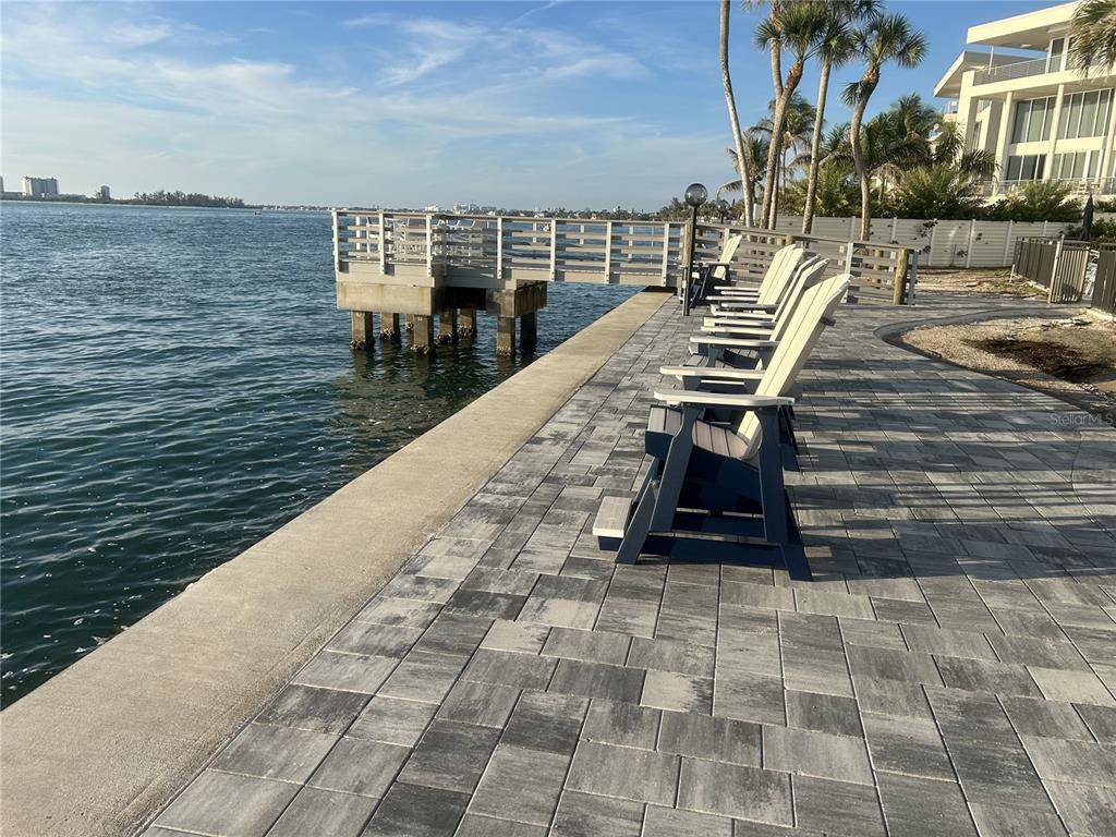 A paved waterfront walkway features a wooden pier and a row of outdoor chairs — 4822 OCEAN BOULEVARD UNIT 3D, SARASOTA, FL