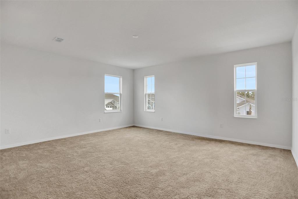 An empty bedroom features light gray walls, beige carpeting, and three windows — 7388 SEA MANATEE STREET, PARRISH, FL