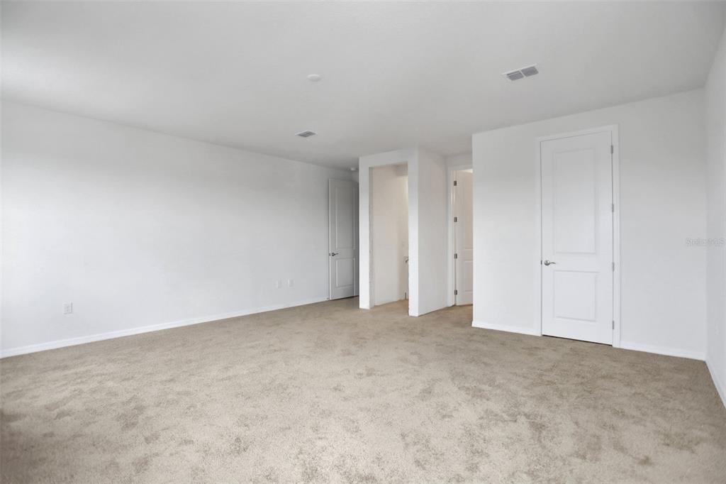 An empty bedroom with beige carpeting, white walls, and multiple interior doors — 7388 SEA MANATEE STREET, PARRISH, FL