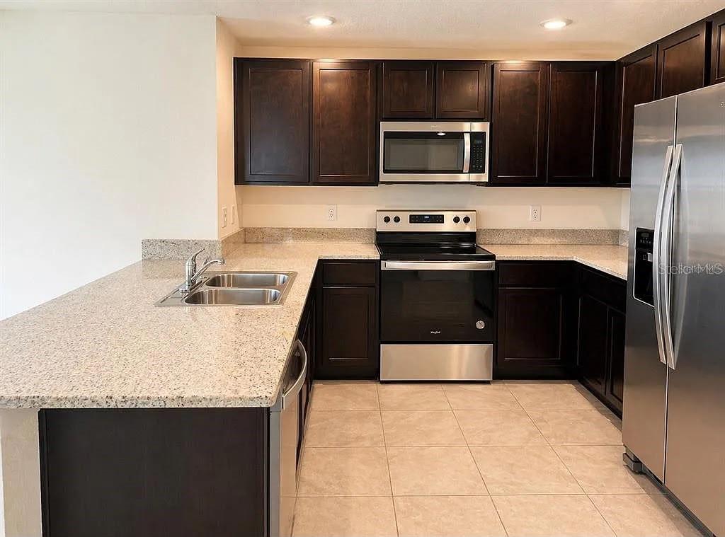 A kitchen features dark wood cabinets, stainless steel appliances, and light granite countertops — 16511 MOSAIC OAR DRIVE, WIMAUMA, FL