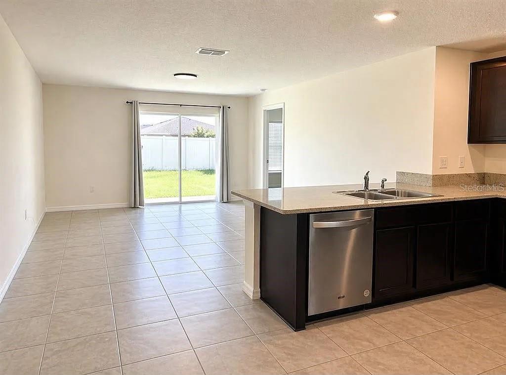 A kitchen with dark cabinets and stainless steel appliances opens to a tiled living area — 16511 MOSAIC OAR DRIVE, WIMAUMA, FL