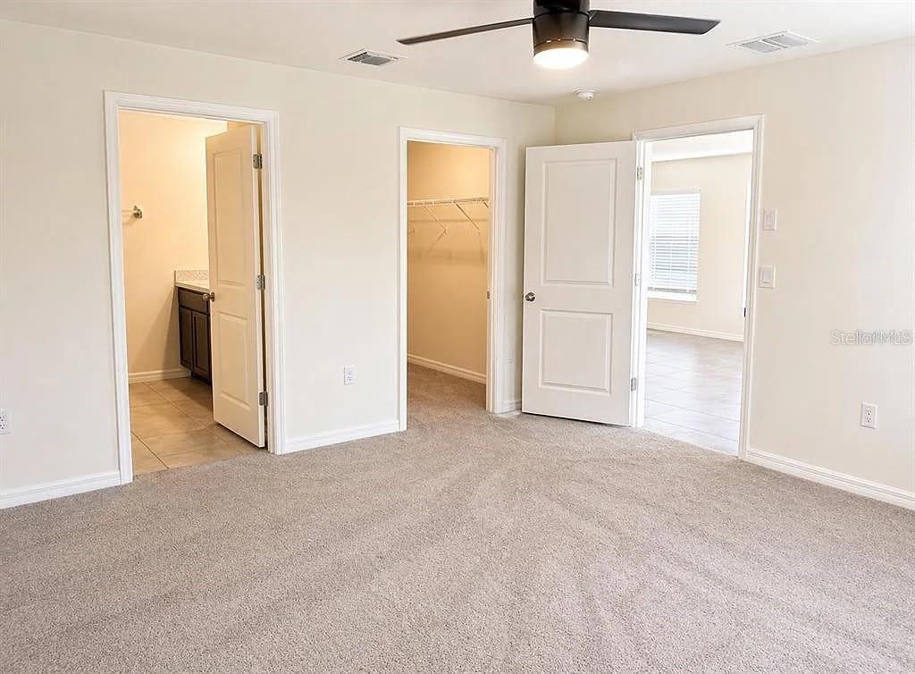 A bedroom with carpeted flooring, a ceiling fan, and doorways leading to a bathroom and closet — 16511 MOSAIC OAR DRIVE, WIMAUMA, FL
