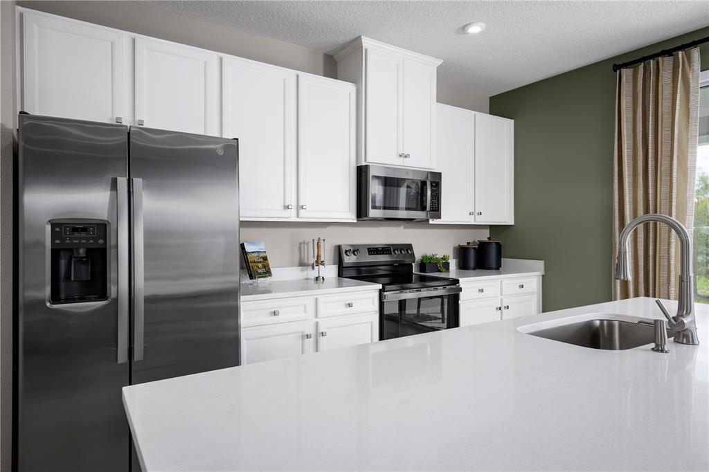 A modern kitchen features white cabinets, stainless steel appliances, and a white quartz island countertop — 1768 KENDALL POINTE PLACE, MELBOURNE, FL