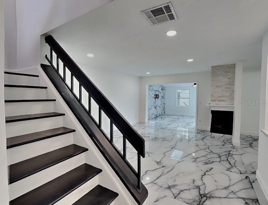 A living room with a fireplace and marble-patterned tile flooring opens to a kitchen — 8212 CITRUS CHASE DRIVE, ORLANDO, FL