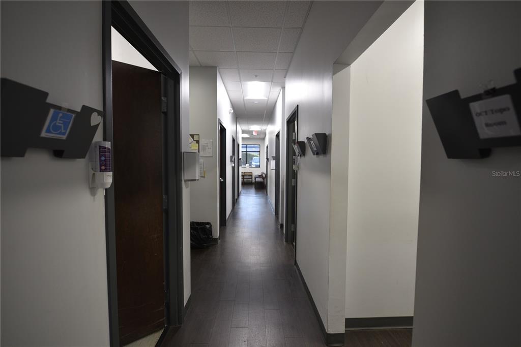 A narrow hallway with dark wood-look flooring leads to a windowed office space at the end — 2460 E HIGHWAY 50, CLERMONT, FL