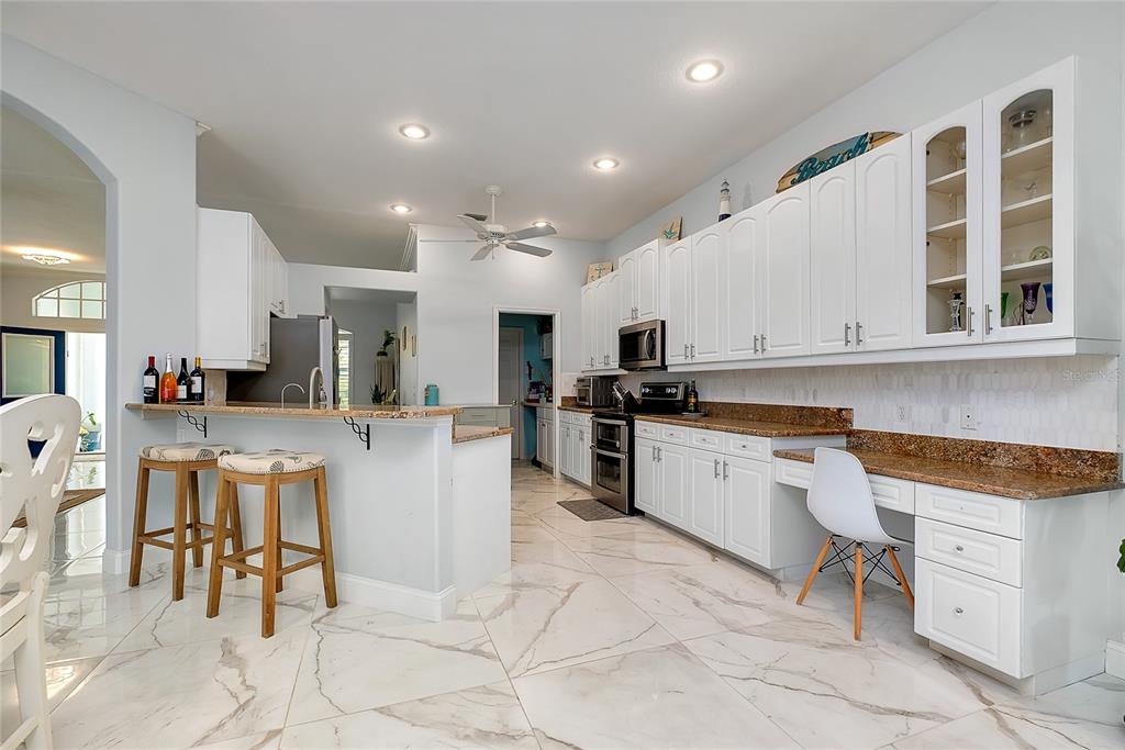 A kitchen features white cabinetry, granite countertops, a breakfast bar with stools, and marble-look flooring — 360 CEDARBROOK COURT, VENICE, FL