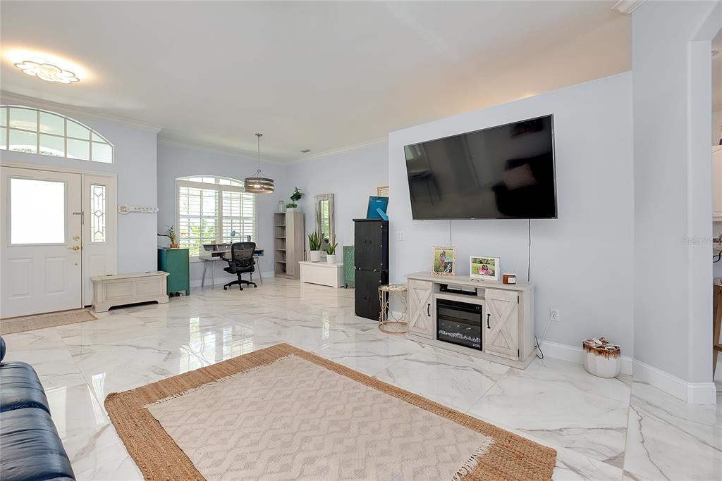 A living room features light blue walls, white marble-look tile flooring, and a wall-mounted television — 360 CEDARBROOK COURT, VENICE, FL
