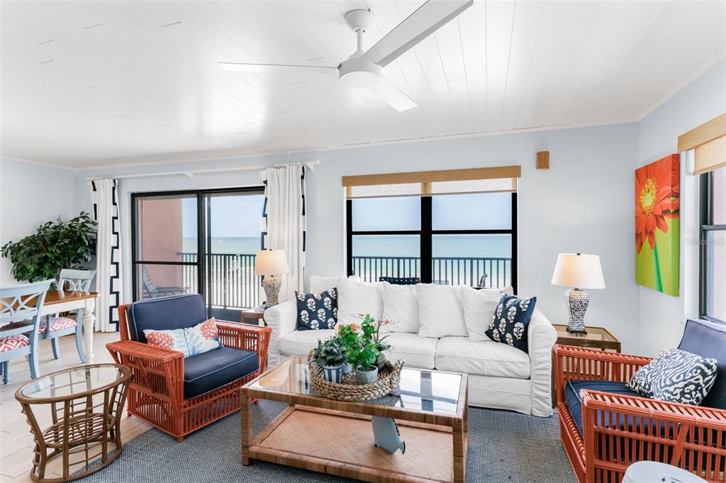 A living room features white furniture, rattan chairs, a glass coffee table, and ocean views — 17334 GULF BOULEVARD UNIT 203, NORTH REDINGTON BEACH, FL
