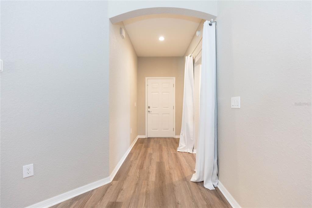 An entryway features wood-look flooring, light gray walls, an arched ceiling, and white curtains — 719 VINEYARD RESERVE COURT, SEFFNER, FL