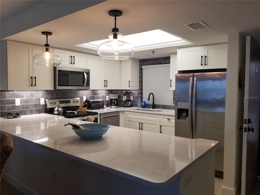 A modern kitchen features white cabinets, stainless steel appliances, a quartz island, and gray tile backsplash — 1001 BENJAMIN FRANKLIN DRIVE UNIT 505, SARASOTA, FL