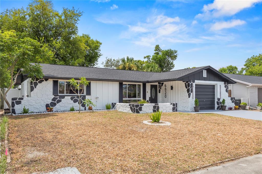 A single-story house features a white exterior with black stone accents and a garage — 6820 EL CAMINO PALOMA STREET, PORT RICHEY, FL