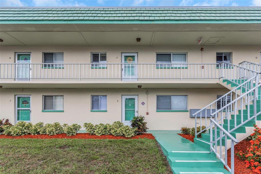 A two-story apartment building exterior features a green roof, white walls, and an outdoor staircase — 2001 GREENBRIAR BOULEVARD UNIT 17, CLEARWATER, FL