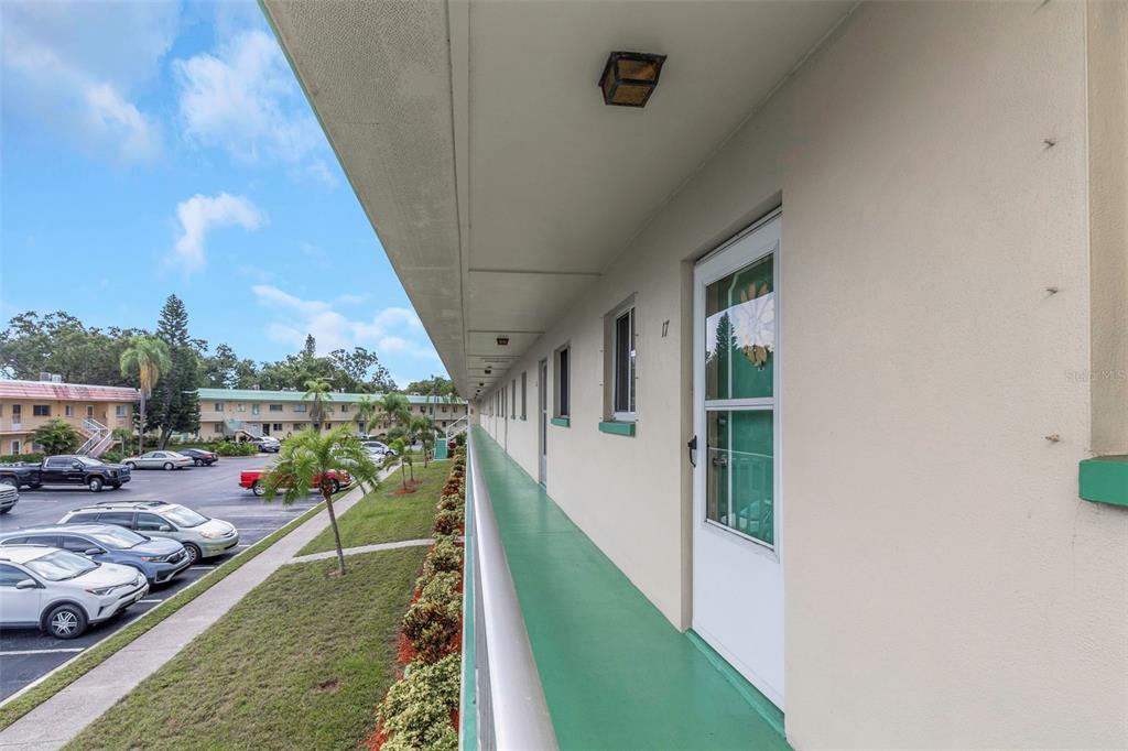 An exterior walkway with a green floor runs along the side of a multi-story apartment building — 2001 GREENBRIAR BOULEVARD UNIT 17, CLEARWATER, FL