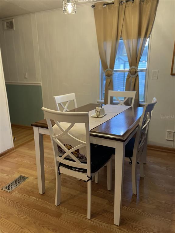 A dining area features a wooden table with white chairs and a window with curtains — 1020 LAUREL COURT W, PALM BAY, FL
