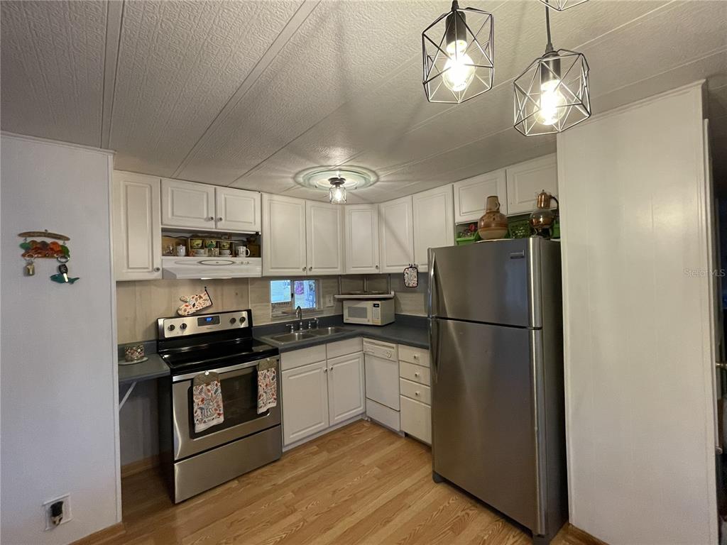 A kitchen features white cabinets, stainless steel appliances, wood-look flooring, and modern geometric pendant lights — 1020 LAUREL COURT W, PALM BAY, FL