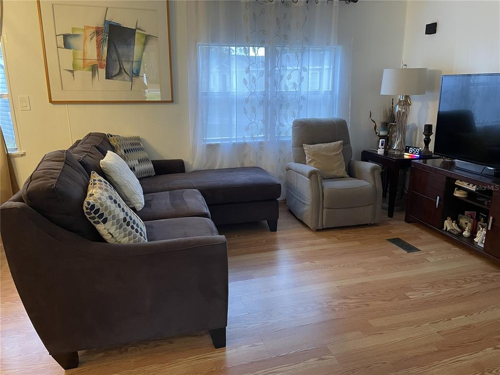 A living room features a dark sectional sofa, a light gray recliner, and wood flooring — 1020 LAUREL COURT W, PALM BAY, FL